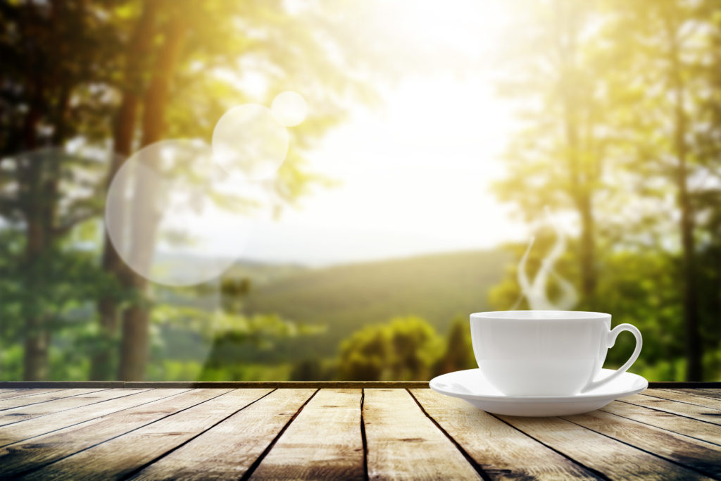 Cup with tea on table over mountains landscape with sunlight. Beauty nature background