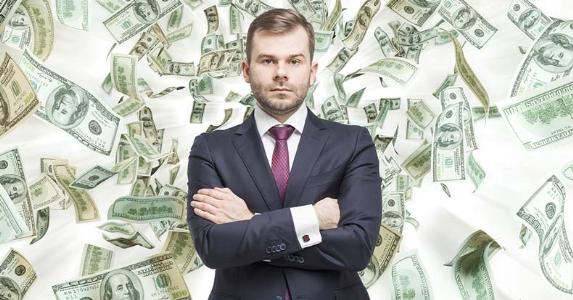serious-businessman-standing-with-money-falling-background_573x300
